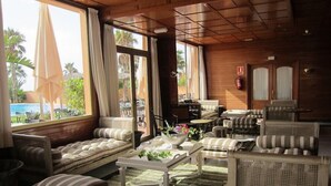 Un vaste espace de détente avec de nombreux sièges, notamment des canapés et des fauteuils, disposés autour d’une table basse centrale. De grandes fenêtres offrent une vue sur l’espace extérieur abritant la piscine.