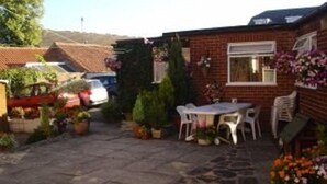 Eine Terrassenfläche mit Steinboden, einem Tisch, Stühlen und Blumentöpfen.