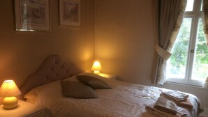 Ein ordentlich gemachtes Bett mit Kissen, einer Nachttischlampe und einem Fenster mit Vorhängen.