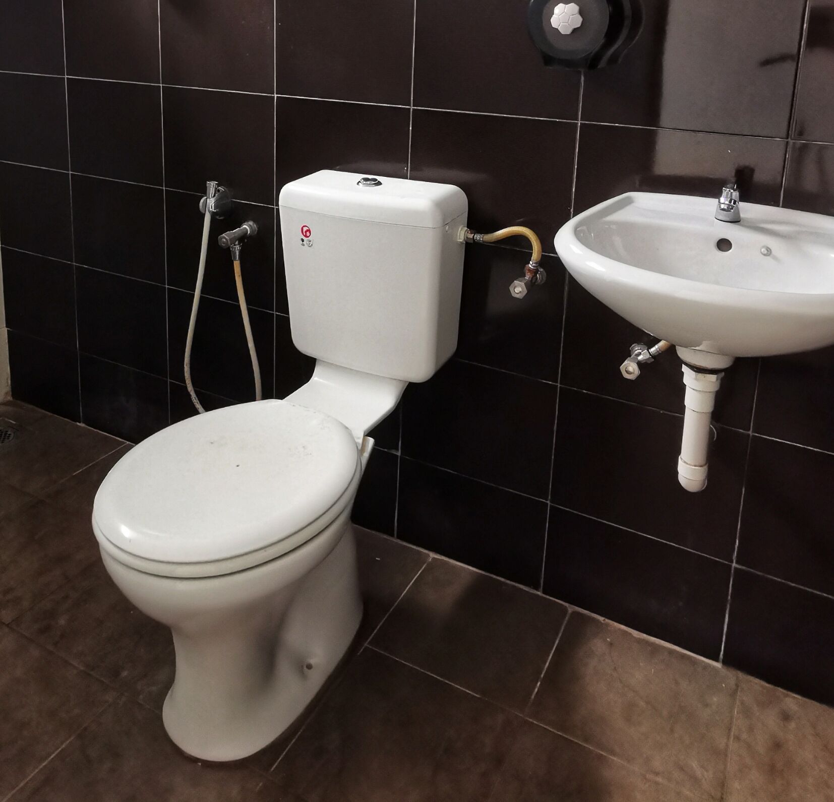 Un inodoro con tanque y asiento blancos, conectado a un lavamanos con pileta blanca y grifo.