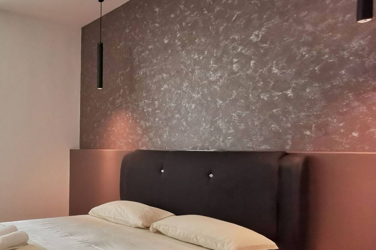 A modern bedroom with a large bed, dark headboard, and a textured wall above.