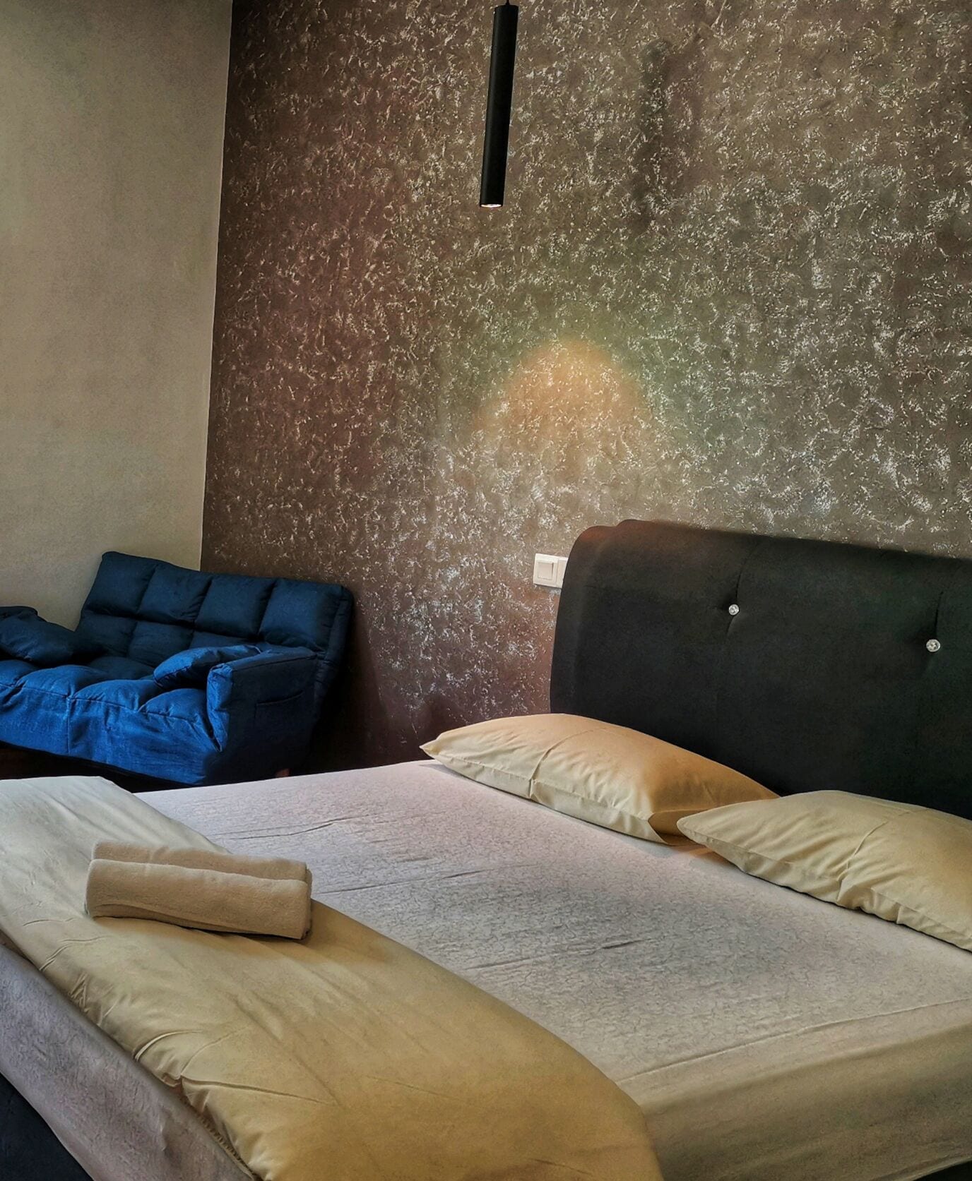 Una habitación con una cama, un sofá azul y una pared con textura.