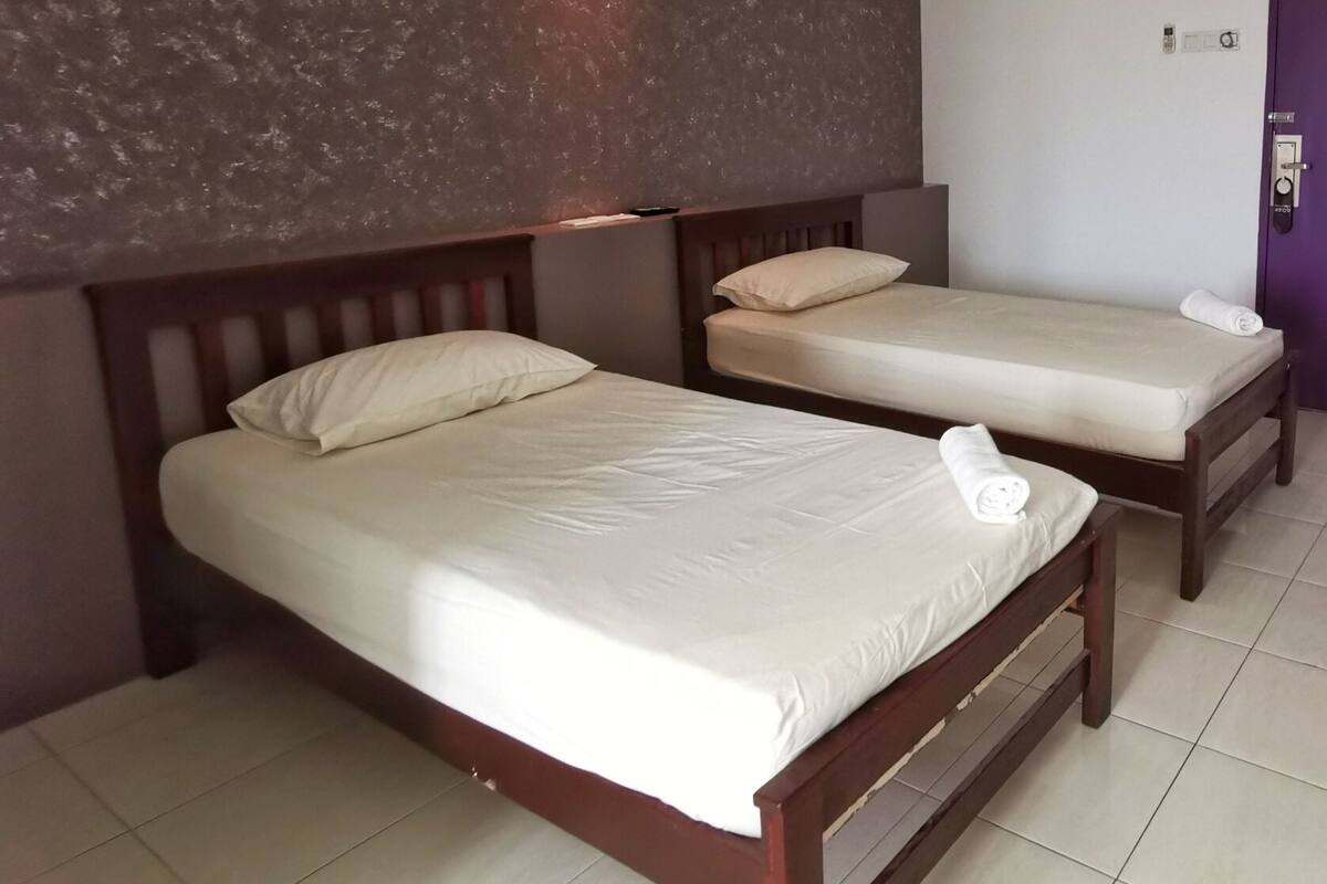 A hotel room with two single beds, a wooden headboard, a textured wall, and a purple door.
