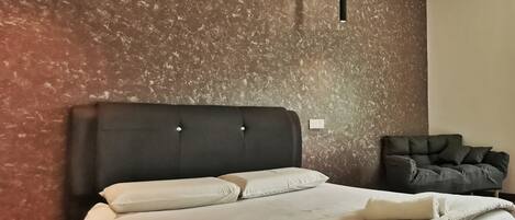 A modern bedroom with a large bed, a dark headboard, a dark sofa, and a textured wall.