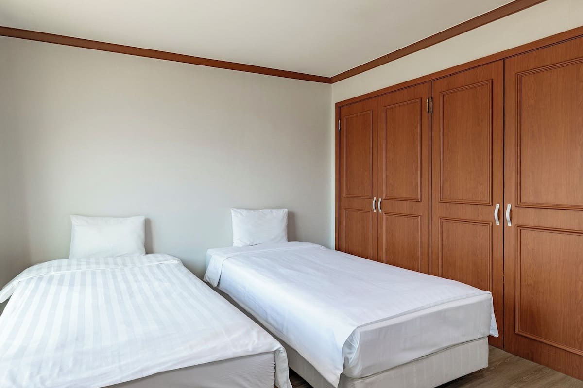 A bedroom with two single beds, wooden wardrobes, and a plain wall.