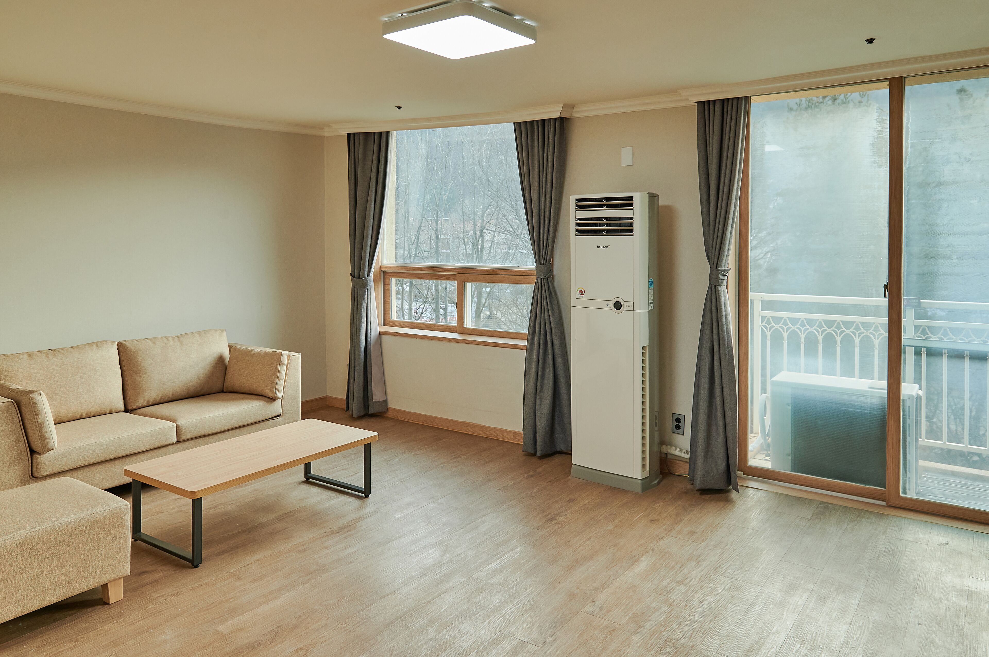 A modern living room with a sofa, a coffee table, and a large window with curtains.
