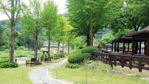 A stone pathway leading to a wooden deck with tables and benches, surrounded by lush greenery and trees.