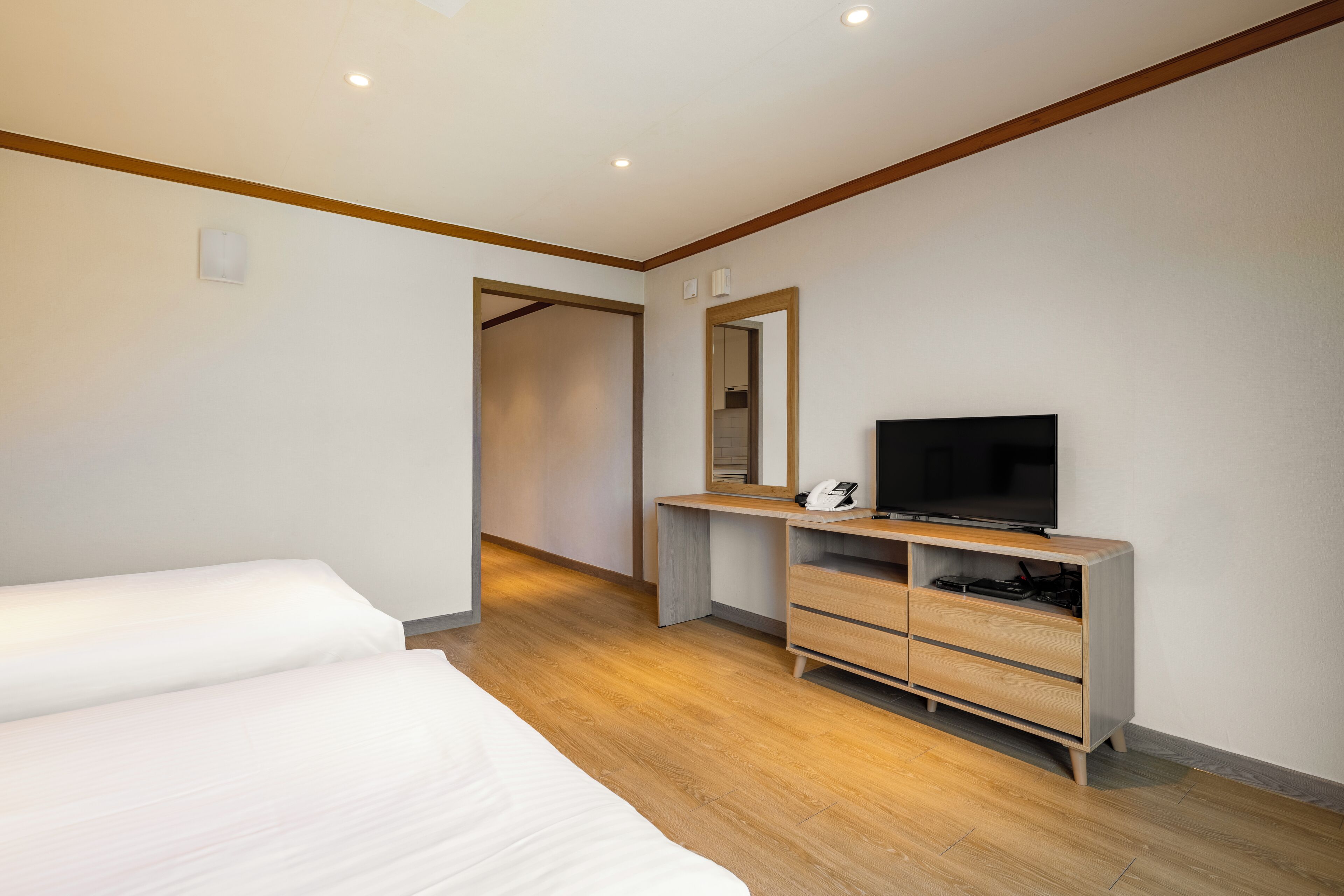 A modern hotel room with a wooden floor, a large bed, a desk with a flat-screen TV, and a wardrobe.