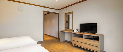 A modern hotel room with a wooden floor, a large bed, a desk with a flat-screen TV, and a wardrobe.