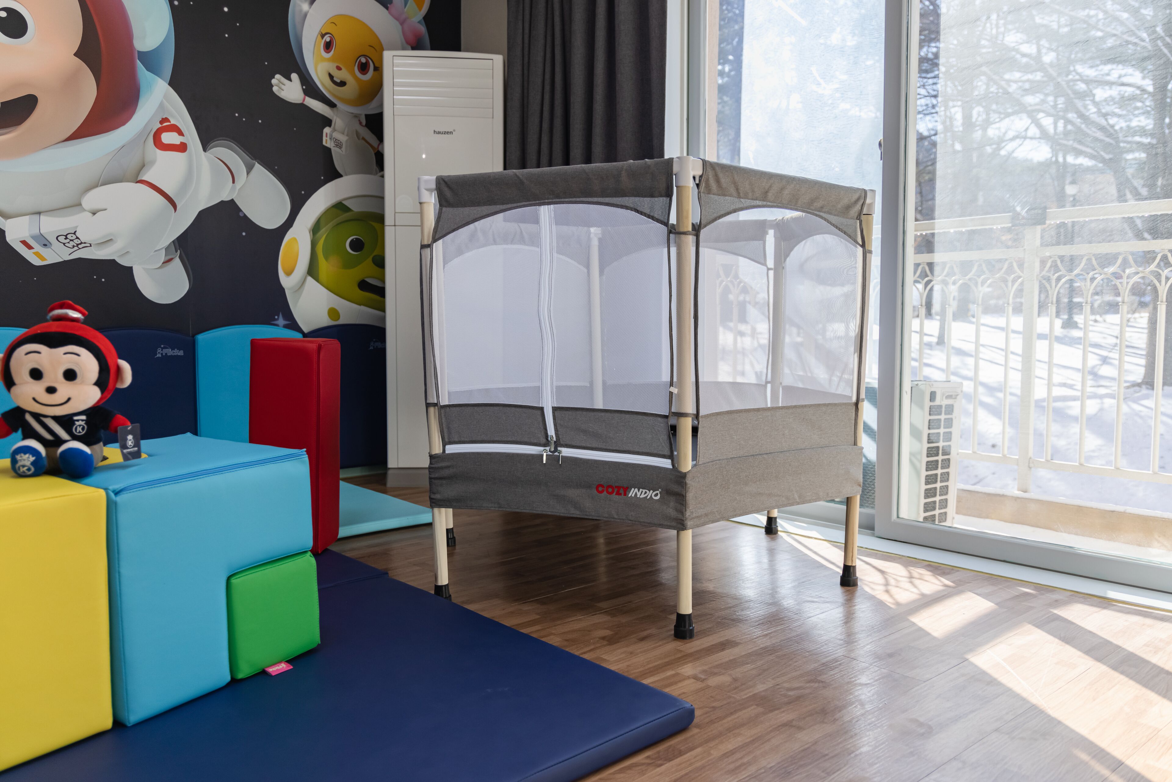 A room with a playpen, colorful blocks, and a window with a view of trees.