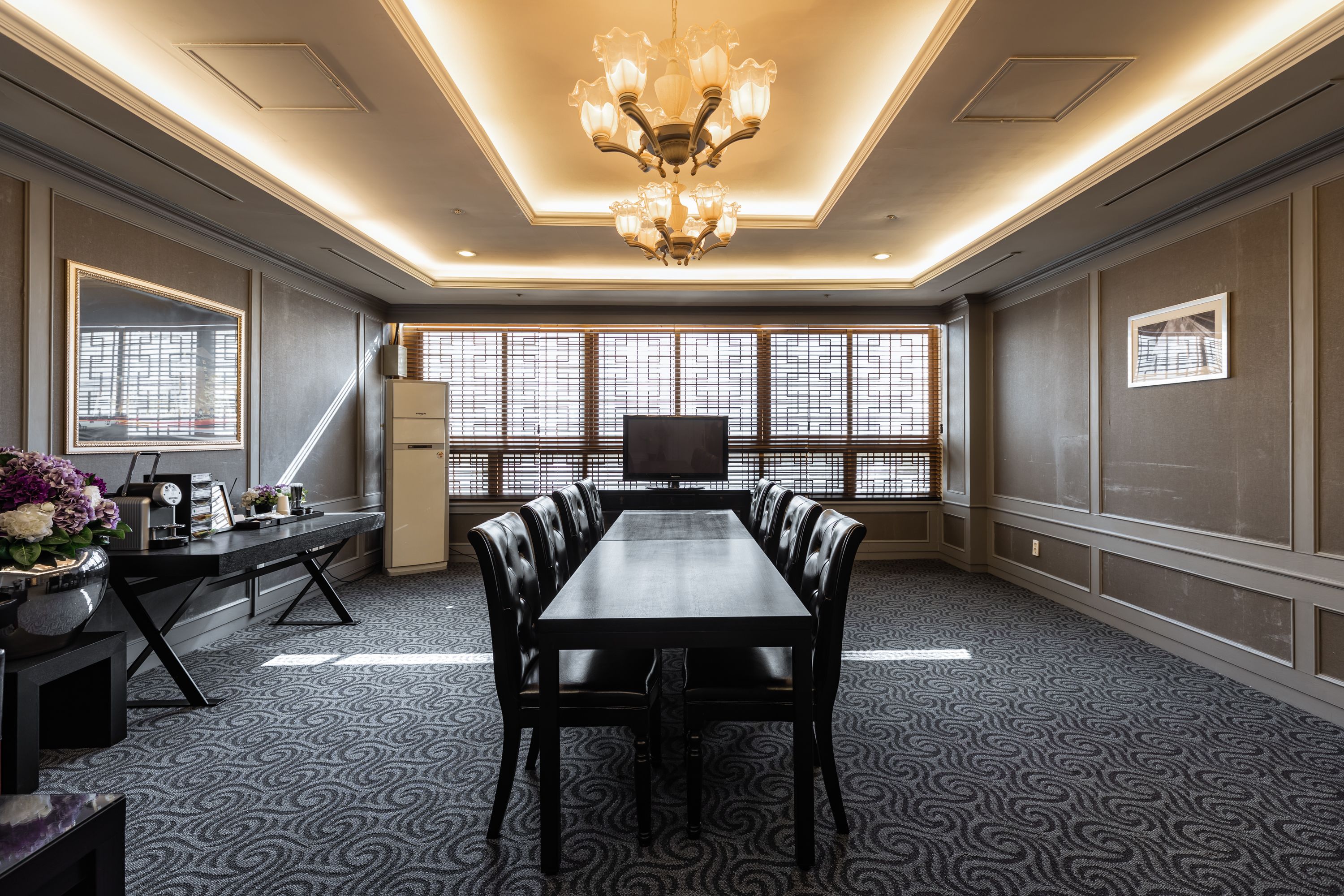 A conference room with a long table, chairs, a chandelier, and large windows.