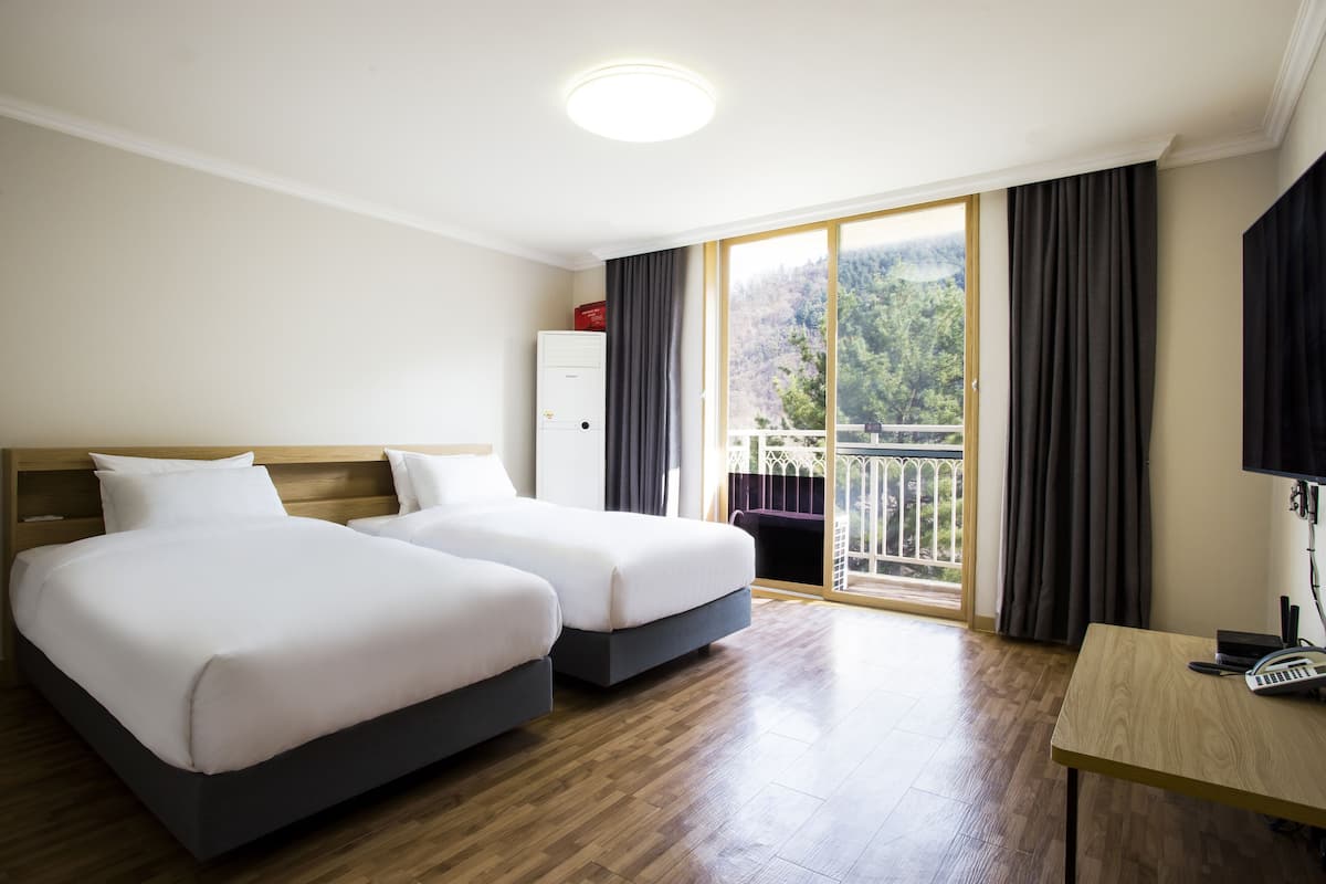A hotel room with two beds, a desk with a telephone and a keyboard, a wardrobe, and a balcony with a view of the outdoors.