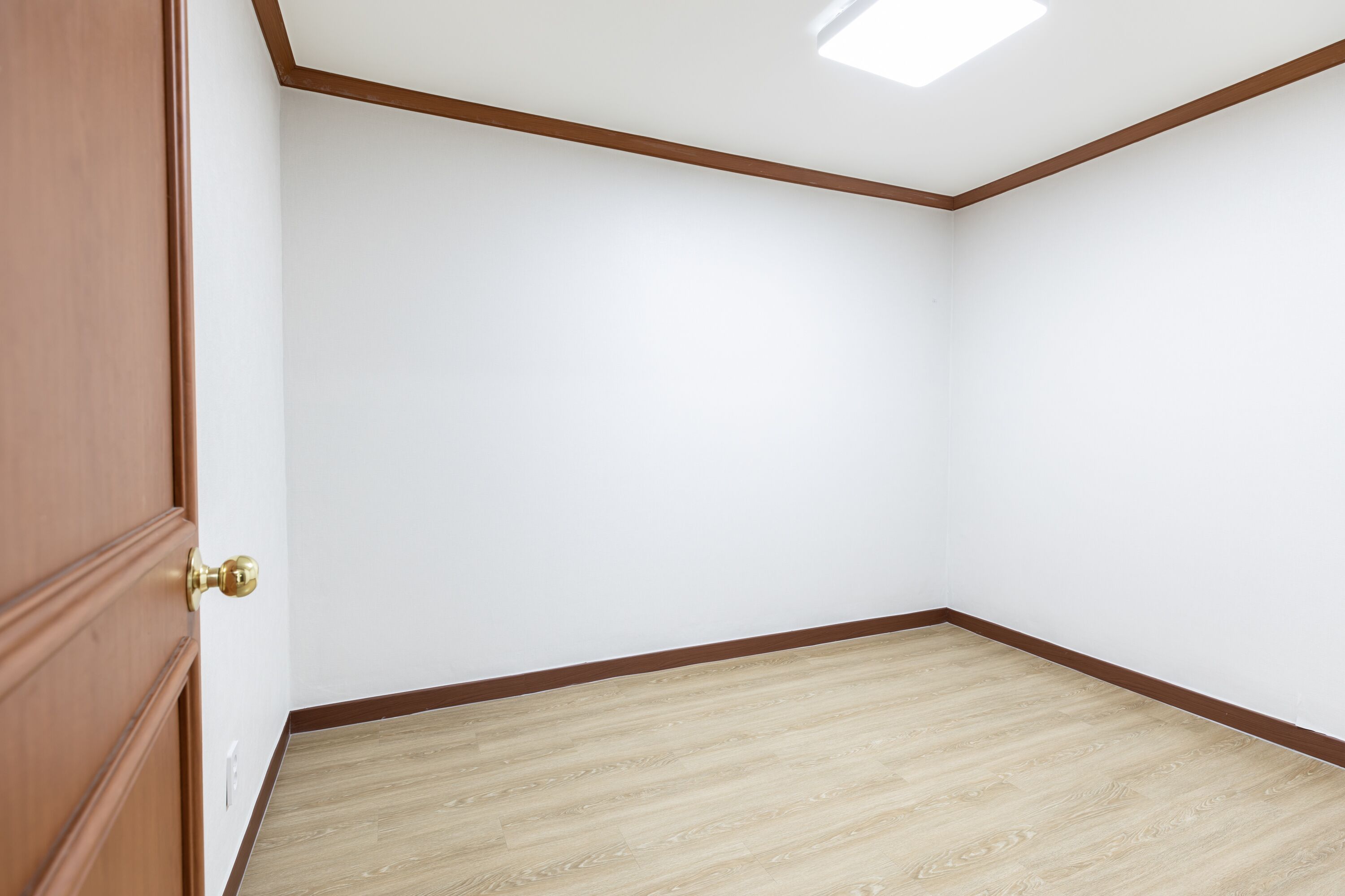 A room with a wooden door, white walls, and a wooden floor.