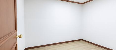 A room with a wooden door, white walls, and a wooden floor.