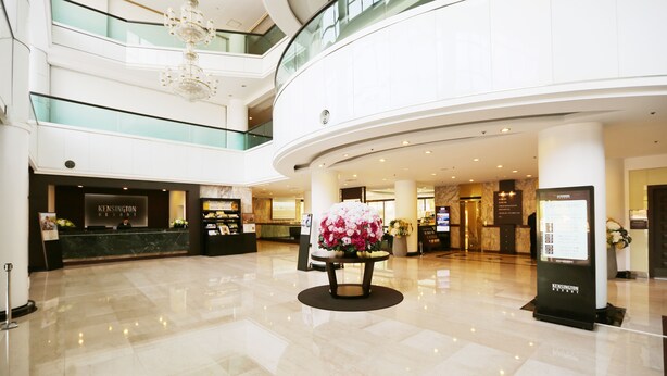 A spacious lobby with a reception desk, a floral centerpiece, and a modern chandelier.
