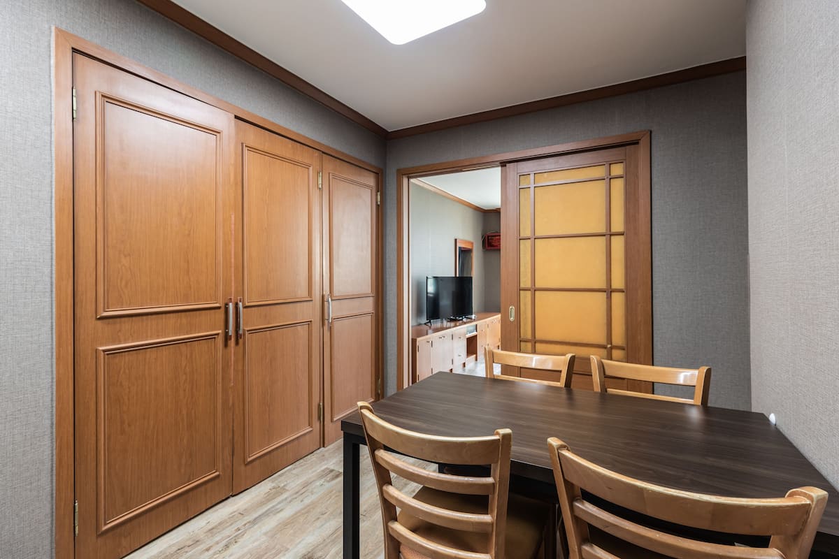 A dining area with a wooden table and chairs, a large wooden wardrobe, and a sliding door with a view into another room.