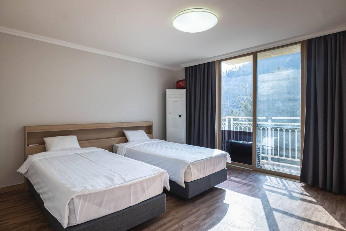 A hotel room with two beds, a wardrobe, a balcony with a railing, and a large window.