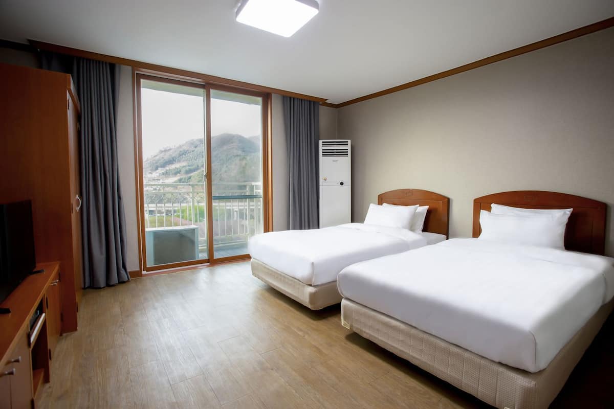 A hotel room with two beds, a TV, a wardrobe, and a balcony with a mountain view.