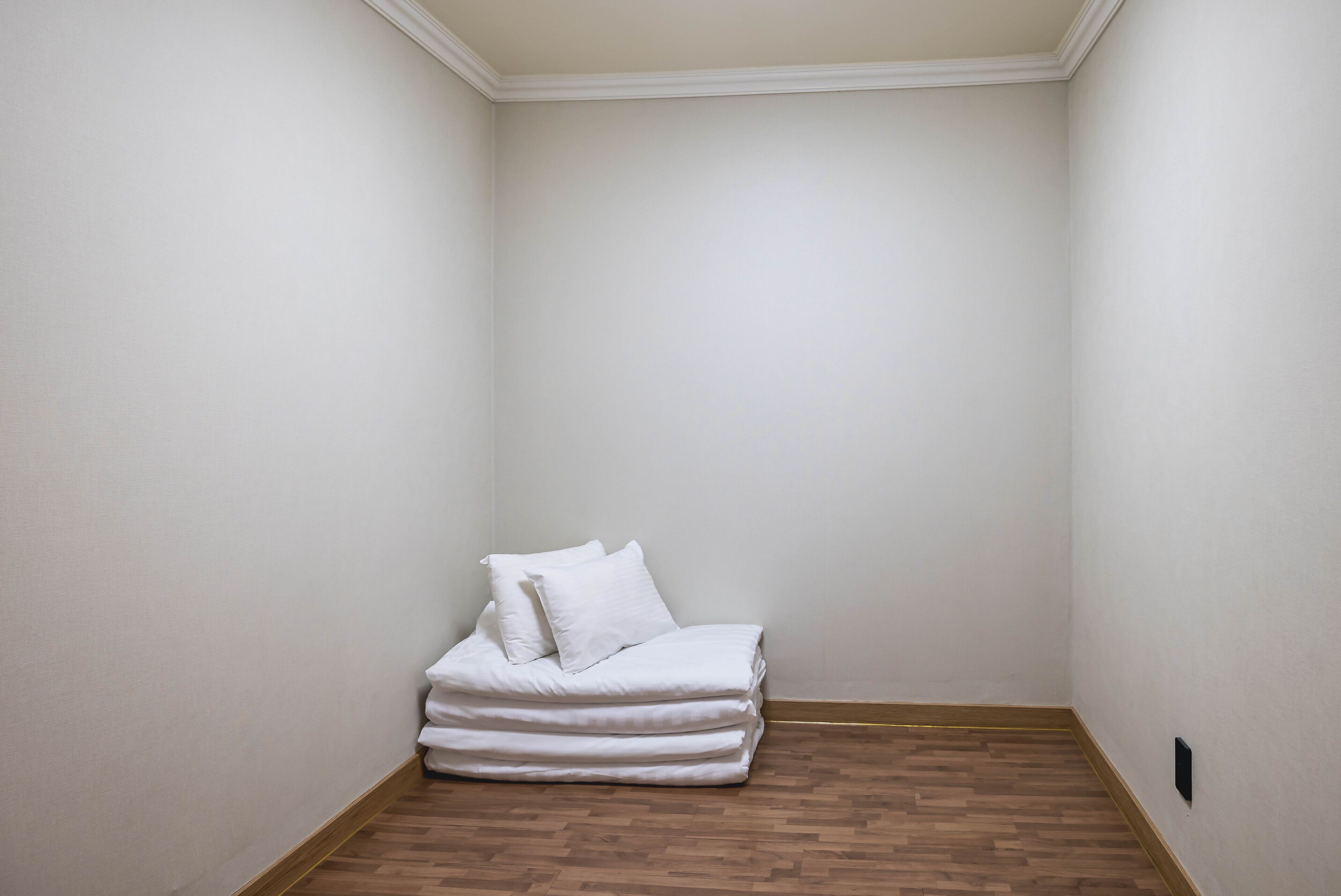 A small, empty room with a neatly made bed and a wooden floor.