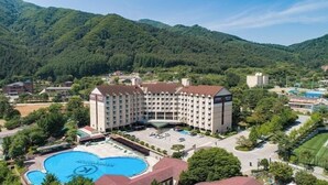 A large hotel with a central courtyard, a swimming pool, and a mountainous backdrop.