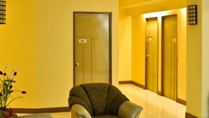 Eine Hotelhalle mit einer Couch, einem Sessel und einem Glastisch. Im Hintergrund sind zwei Türen zu sehen, eine davon ist mit der Nummer 221 gekennzeichnet.