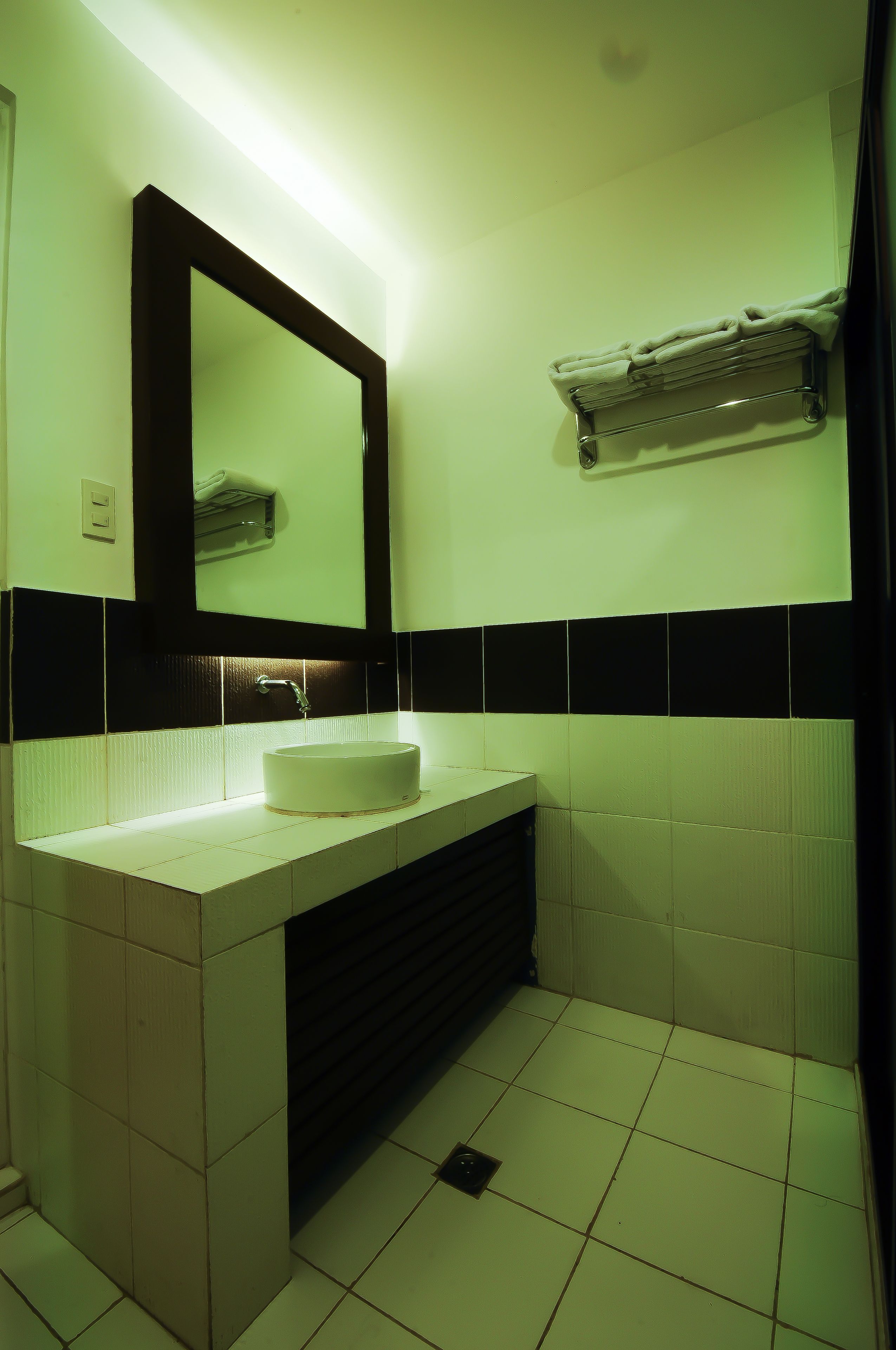 Un baño con lavamanos blanco, azulejos blanco y negro, un espejo y un perchero para toallas.