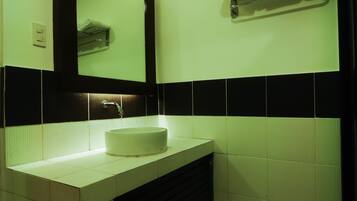 Un baño con lavamanos blanco, azulejos blanco y negro, un espejo y un perchero para toallas.