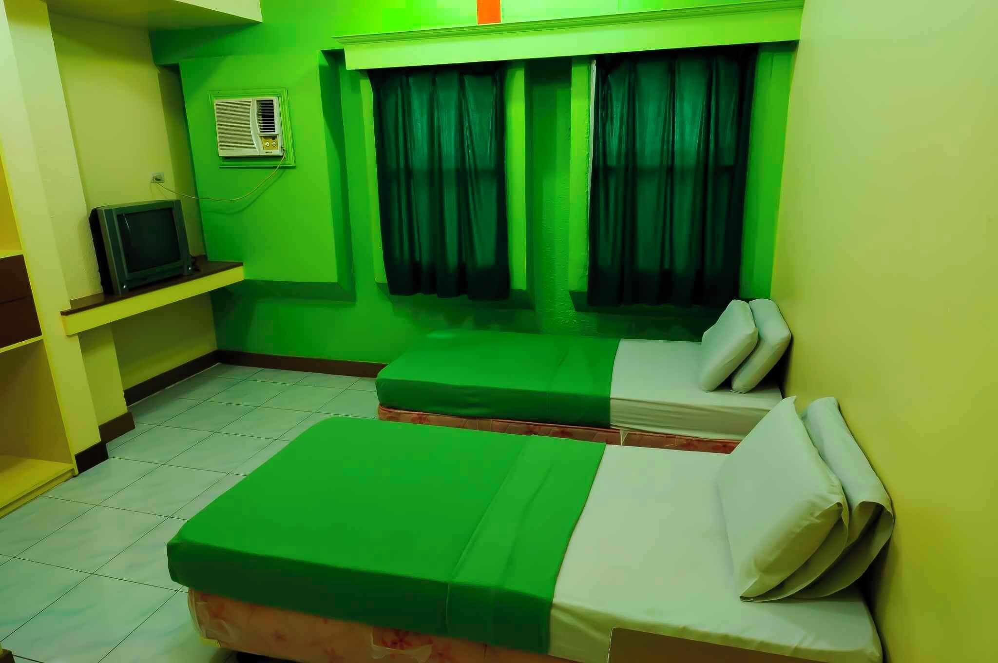 A room with a bed, a small table, a television, and a window with curtains.