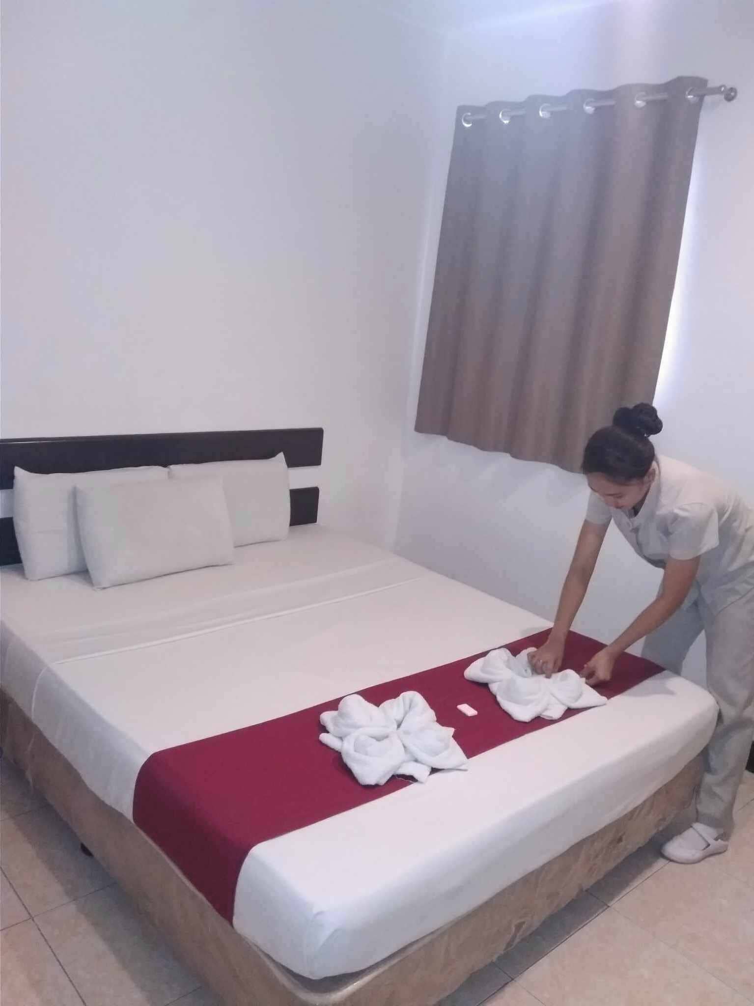 Una cama bien hecha con una manta roja y almohadas blancas.