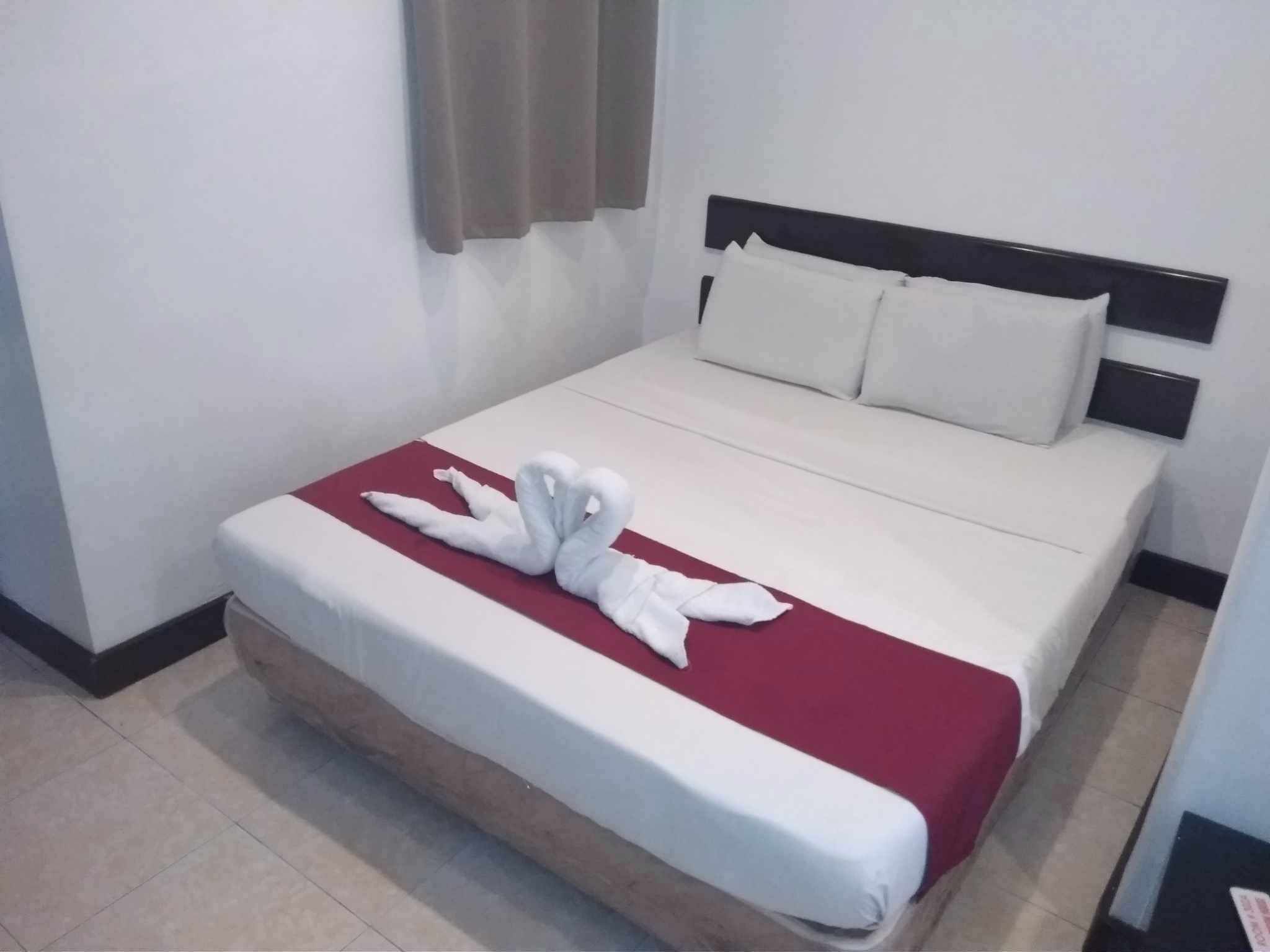 Quarto de hotel com cama, roupa de cama branca, manta vermelha e arranjo de toalha em forma de cisne.