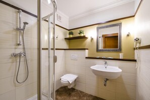 A bathroom with a glass-enclosed shower, a white sink, and a small toilet. - American House Baletowa (Warsaw)