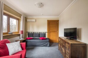 A bedroom with a bed, a TV, a dresser, a window with curtains, and a radiator. - American House Baletowa (Warsaw)