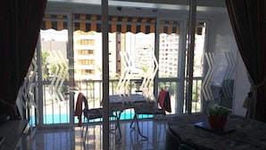 A balcony with a glass door, a table, and chairs. - Apartamentos Bermudas (Benidorm)