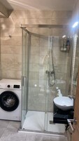 A compact bathroom with a glass-enclosed shower, a washing machine, and a sink.