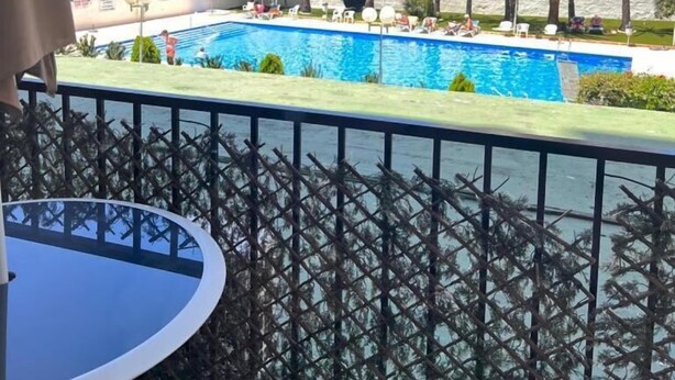 A pool area with a view of a tall building and palm trees. - Apartamentos Bermudas (Benidorm)