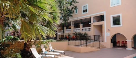 A poolside area with lounge chairs, a palm tree, and a building with multiple windows and balconies.