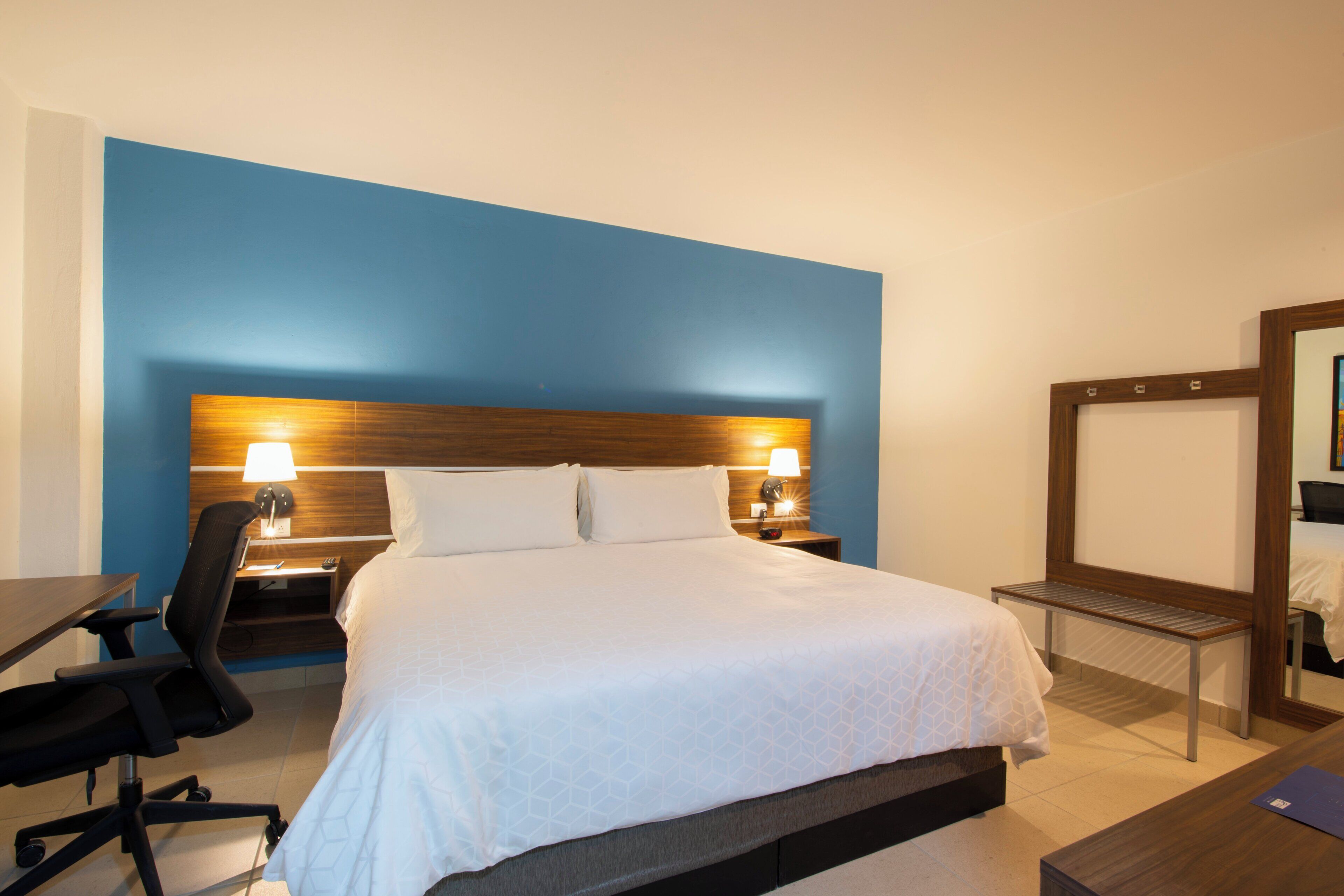 Una habitación de hotel con cama, mesitas de noche, escritorio, silla y espejo.