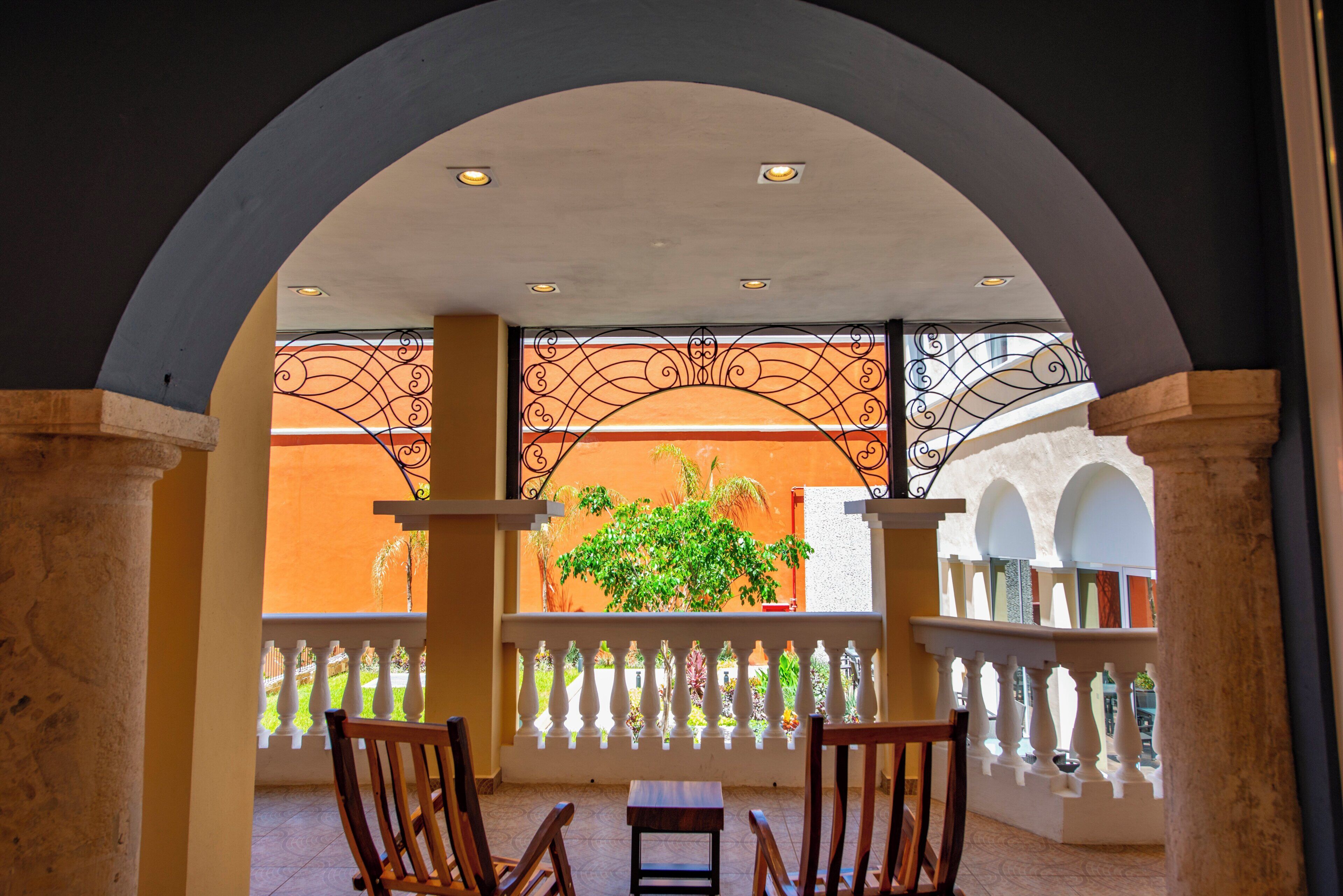 A covered outdoor seating area with a view of a garden and a building with orange walls.