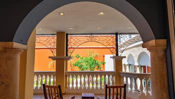 A covered outdoor seating area with a view of a garden and a building with orange walls.