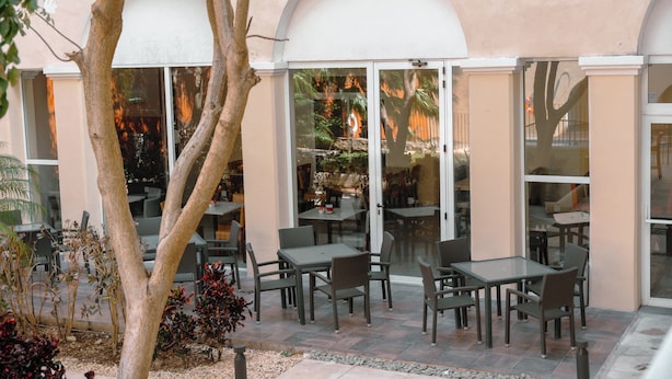 An outdoor patio area with tables and chairs, surrounded by glass doors and windows, and a tree in the foreground.