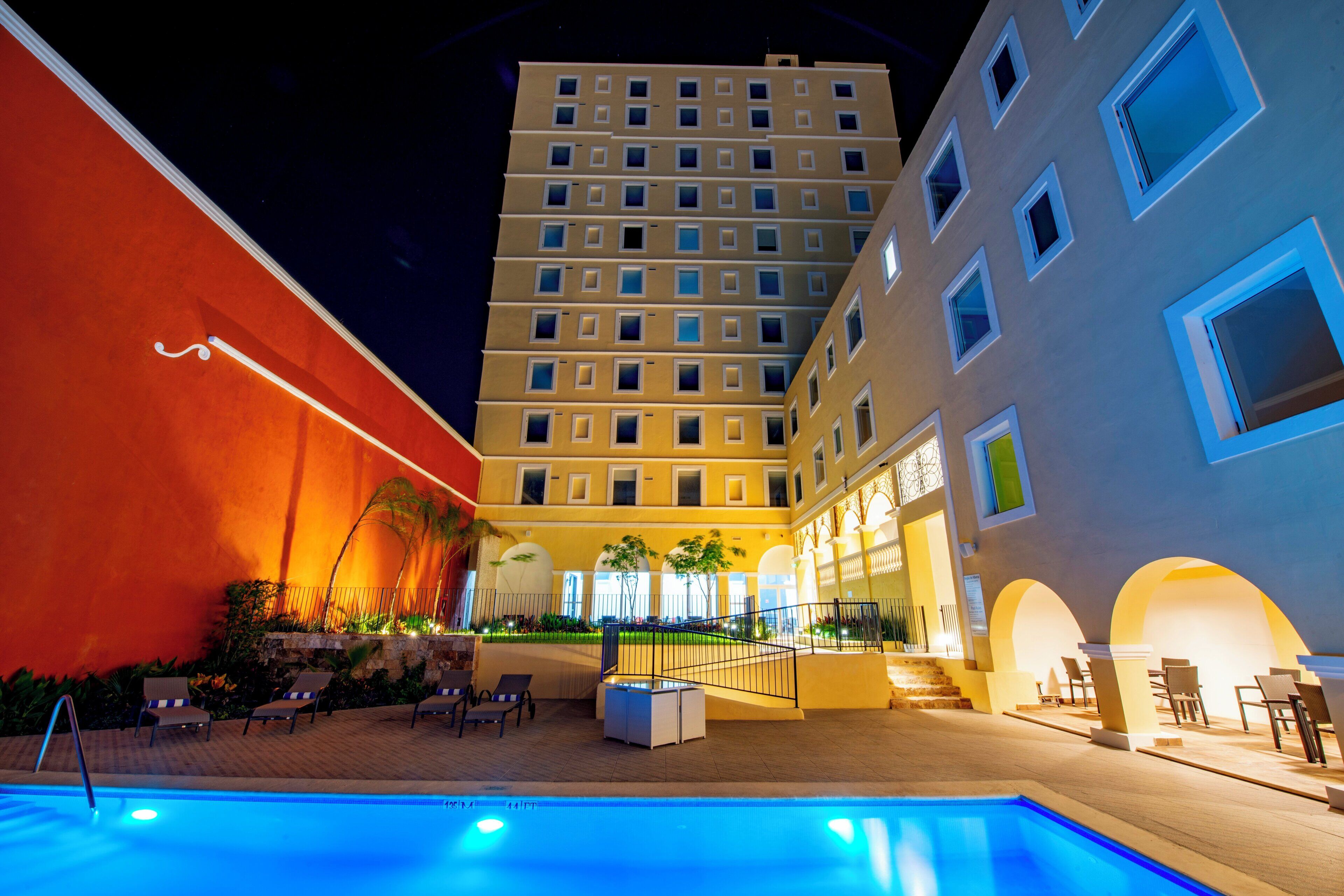 Un hotel amb piscina, zones d'estar a l'aire lliure i un edifici d'alguns pisos amb balcons.