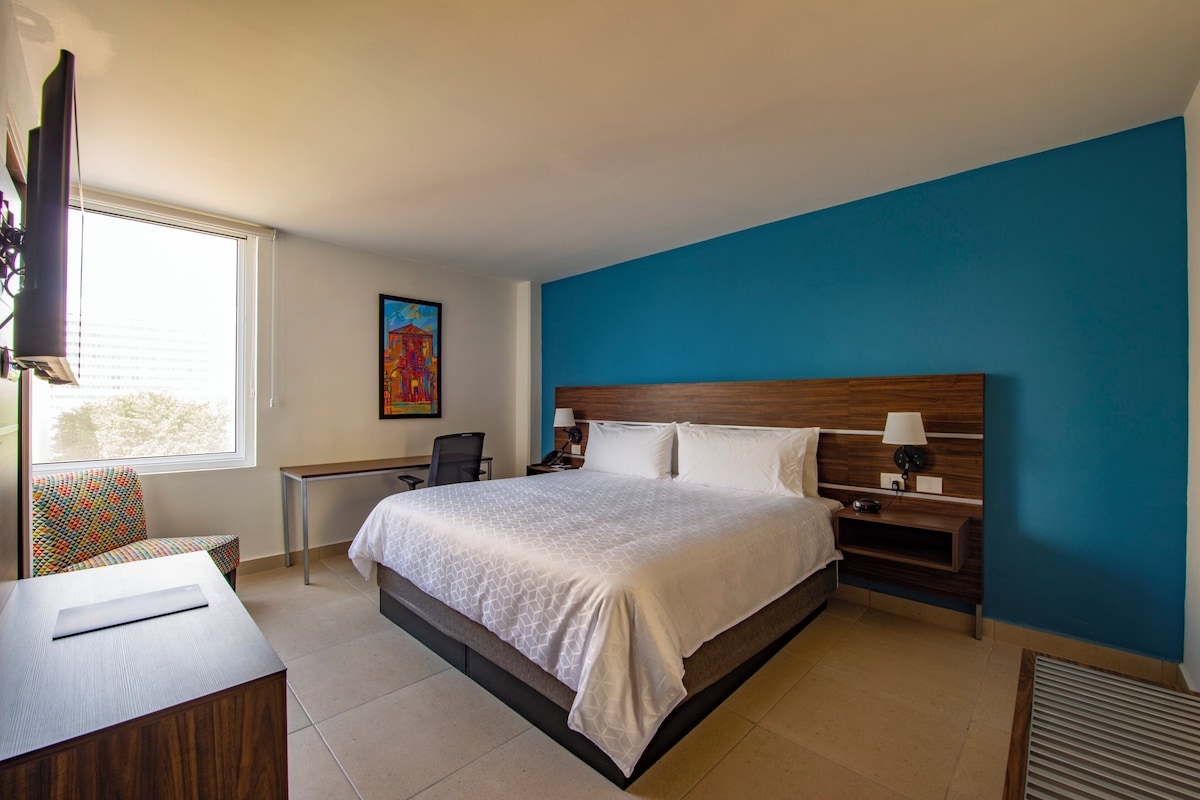 Una habitación de hotel con una cama, mesitas de noche, un escritorio y una silla.