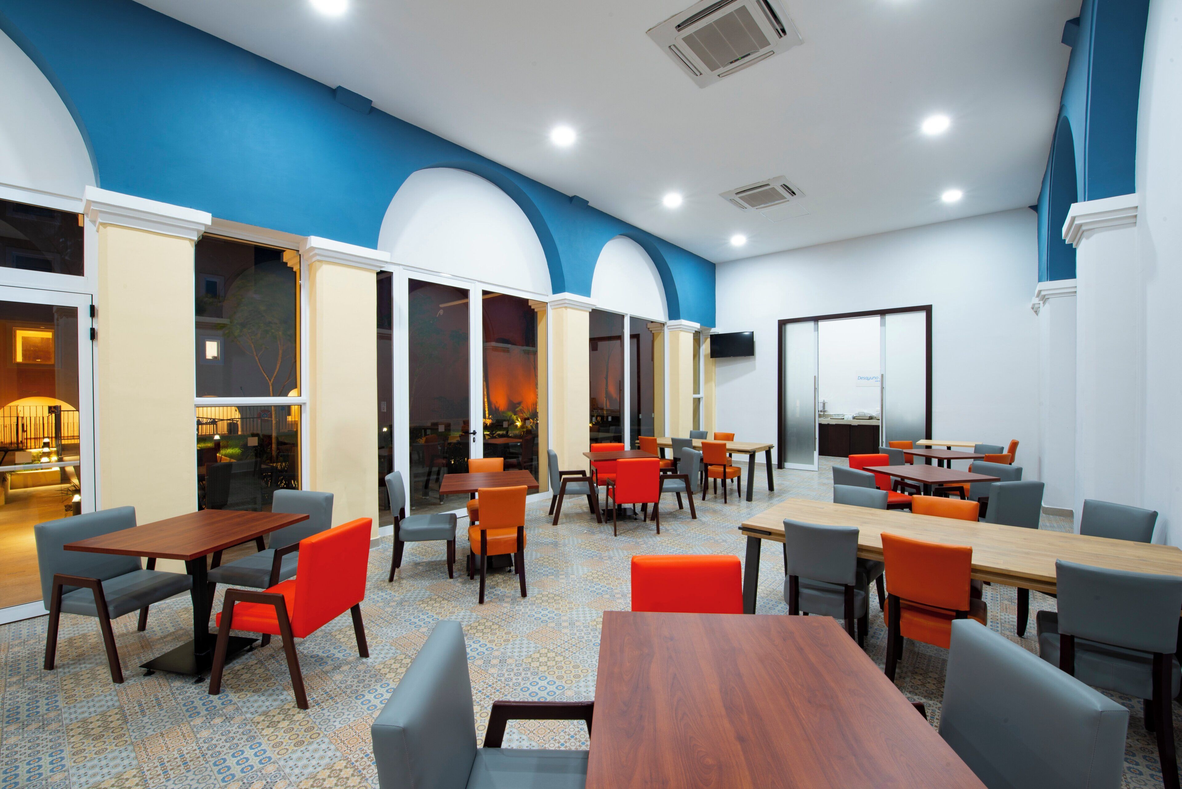A modern dining area with multiple tables and chairs, large windows, and a blue accent wall.