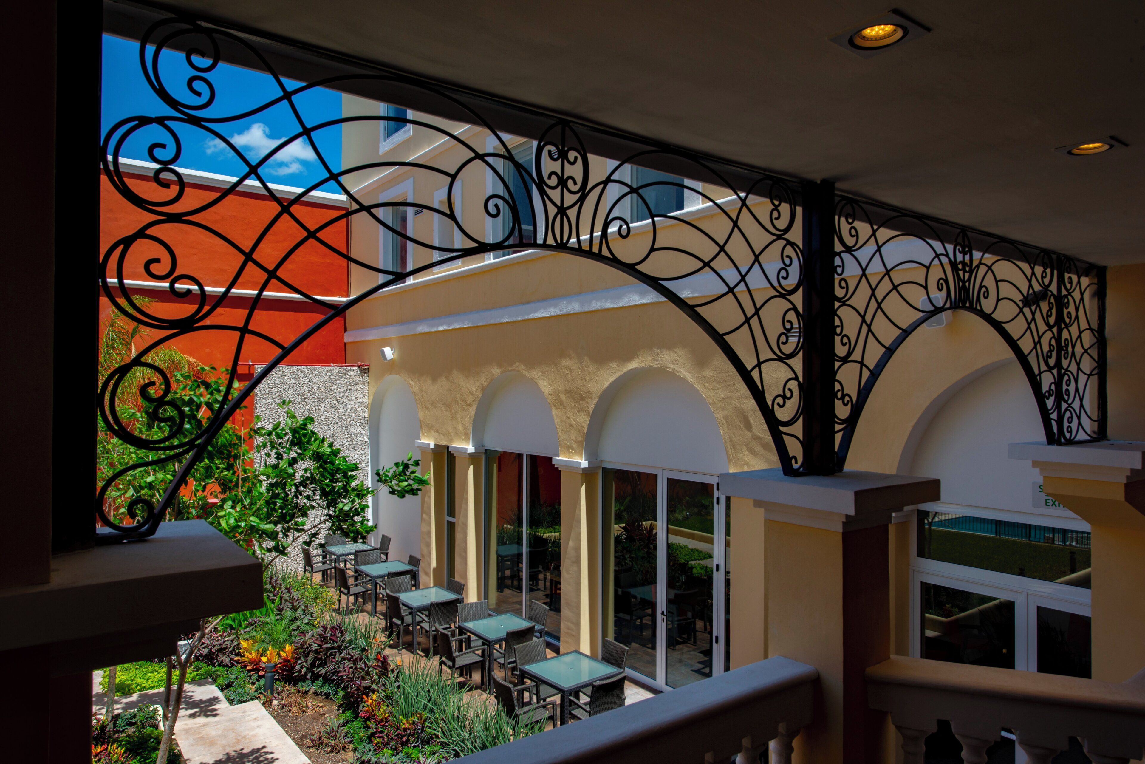 An outdoor seating area with tables and chairs, surrounded by a decorative wrought iron railing.