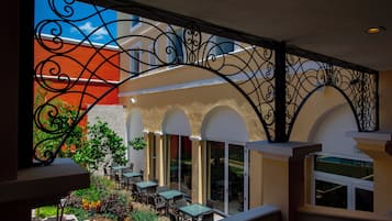 An outdoor seating area with tables and chairs, surrounded by a decorative wrought iron railing.