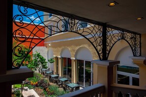Un área de estar al aire libre con mesas y sillas, rodeada por una barandilla decorativa de hierro forjado.