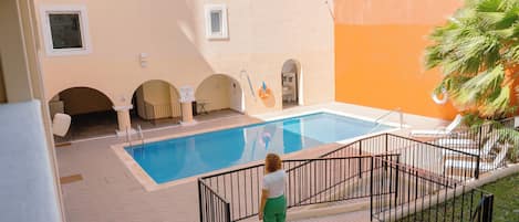 A swimming pool area with a tiled deck, a small covered seating area, and a palm tree.
