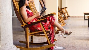 A person seated on a rocking chair reading a book in a well-lit indoor area with tiled flooring.