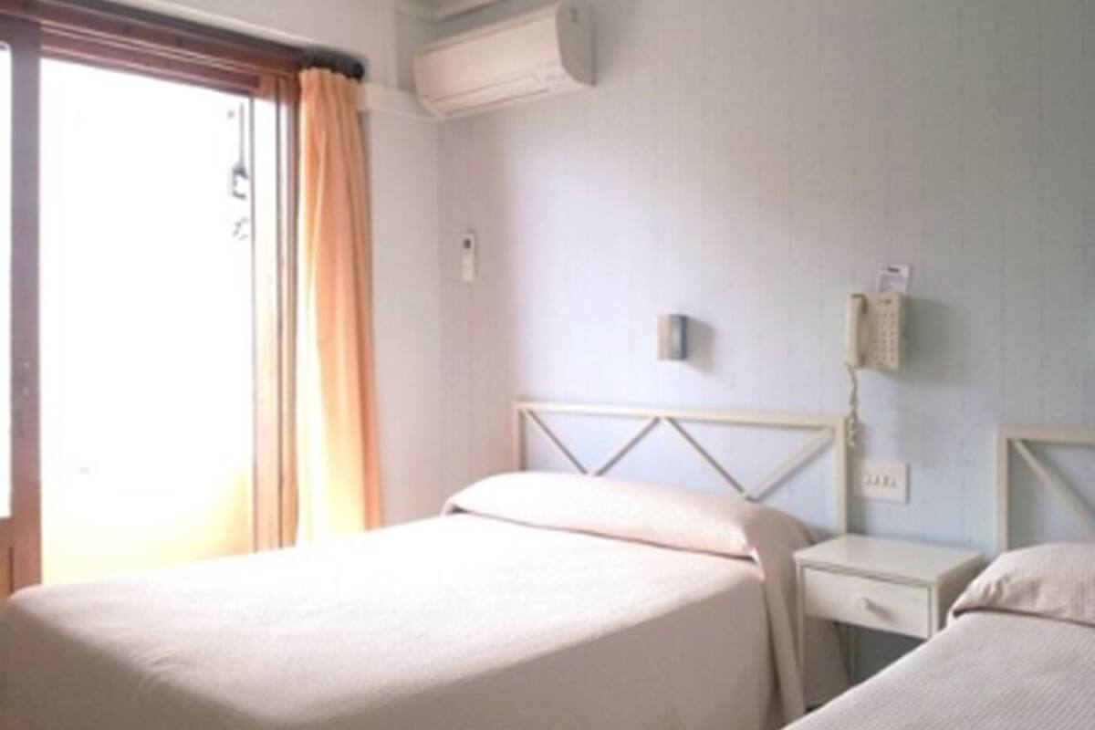 Habitación de hotel con una cama individual, una mesita de noche y un teléfono instalado en la pared.