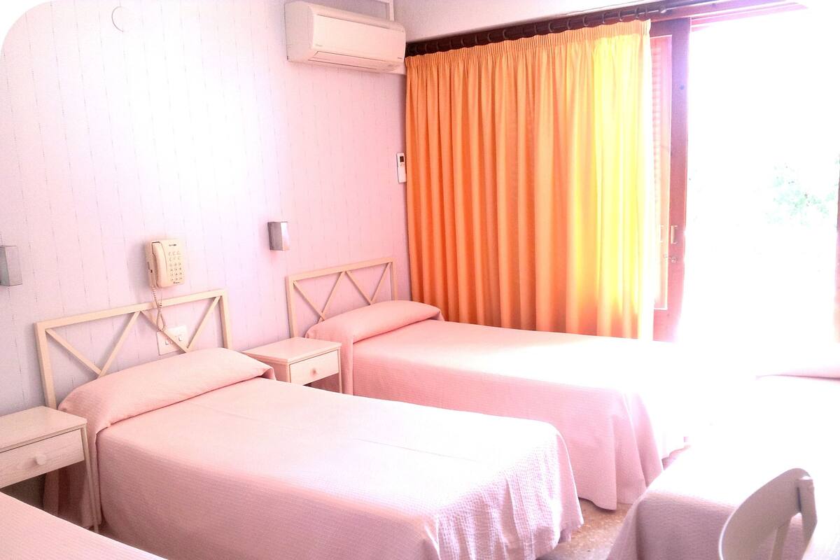 Una habitación de hotel con dos camas, teléfono junto a la cama, equipo de aire acondicionado y una ventana con cortinas.